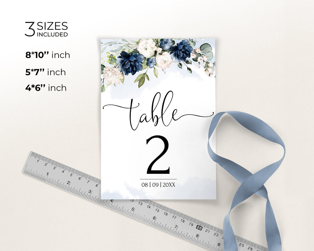 Table number card with floral design and ribbon, accompanied by a ruler for size reference.
