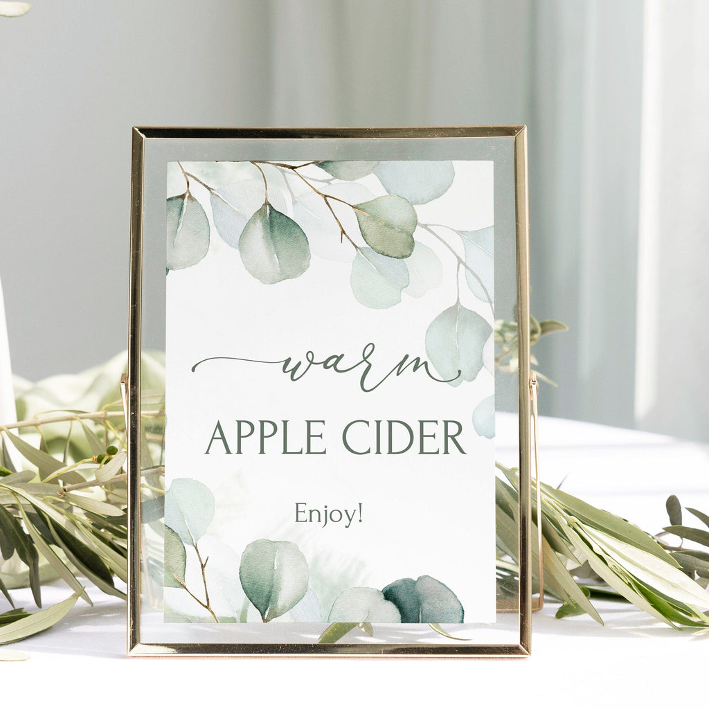 A digital dessert bar sign with the text 'warm APPLE CIDER Enjoy!' written in script, surrounded by eucalyptus leaf illustrations, framed in a gold border.