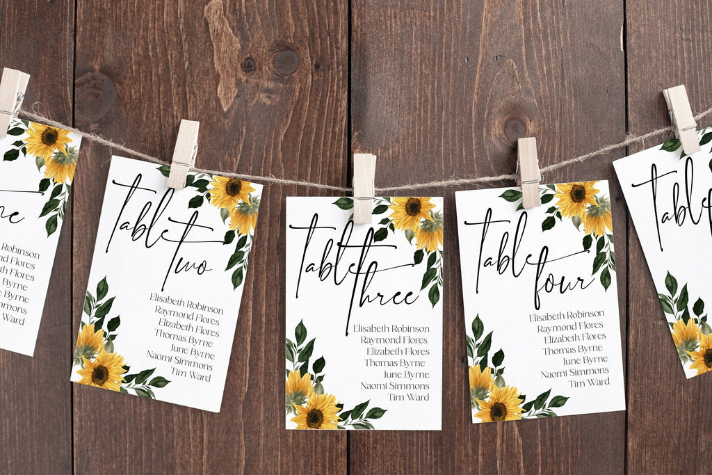 Hanging sunflower-themed seating chart cards with the word 'TABLE' printed on them, displayed on a wooden background.