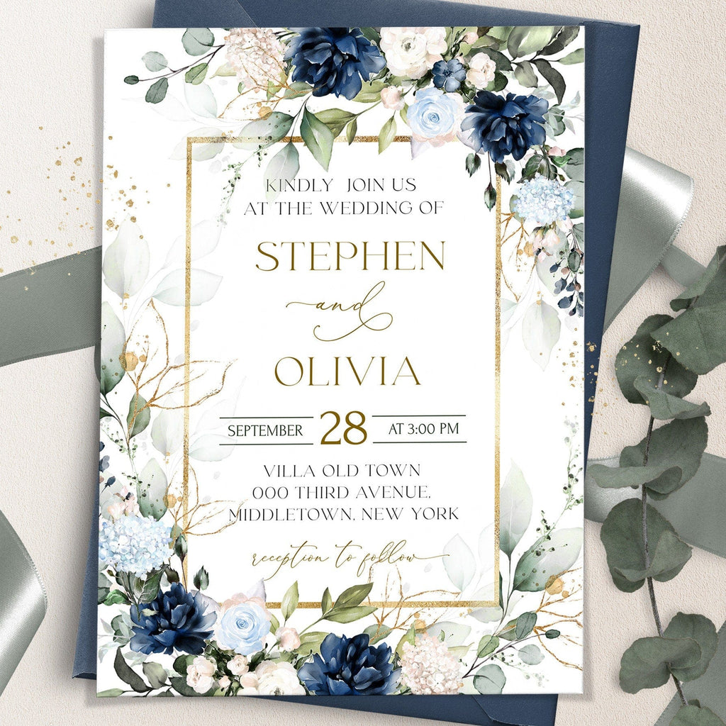 A printed wedding invitation with a floral design, royal blue text, and gold accents, displayed on a table with a blue flower and a golden card holder.