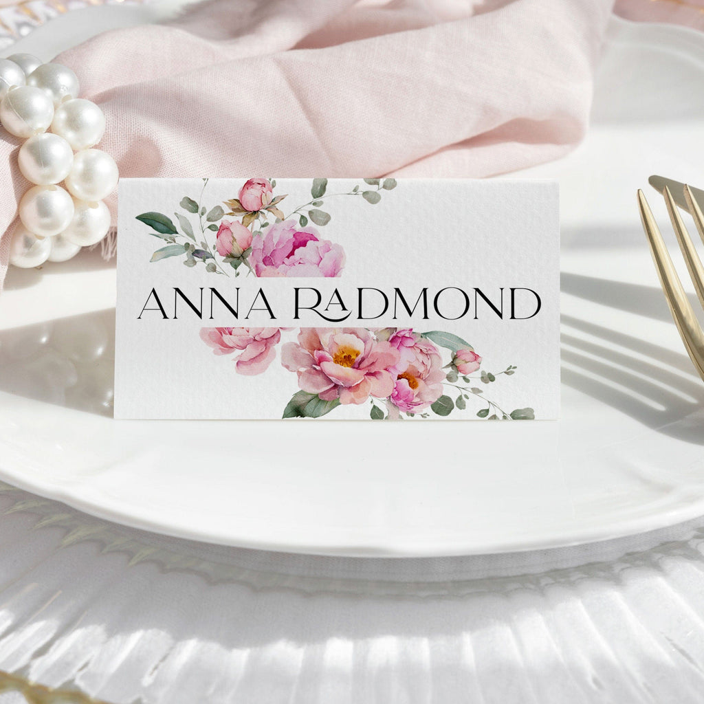 A folded pink place card with a floral design featuring peony blooms, customized with the name 'Anna Radmond'.