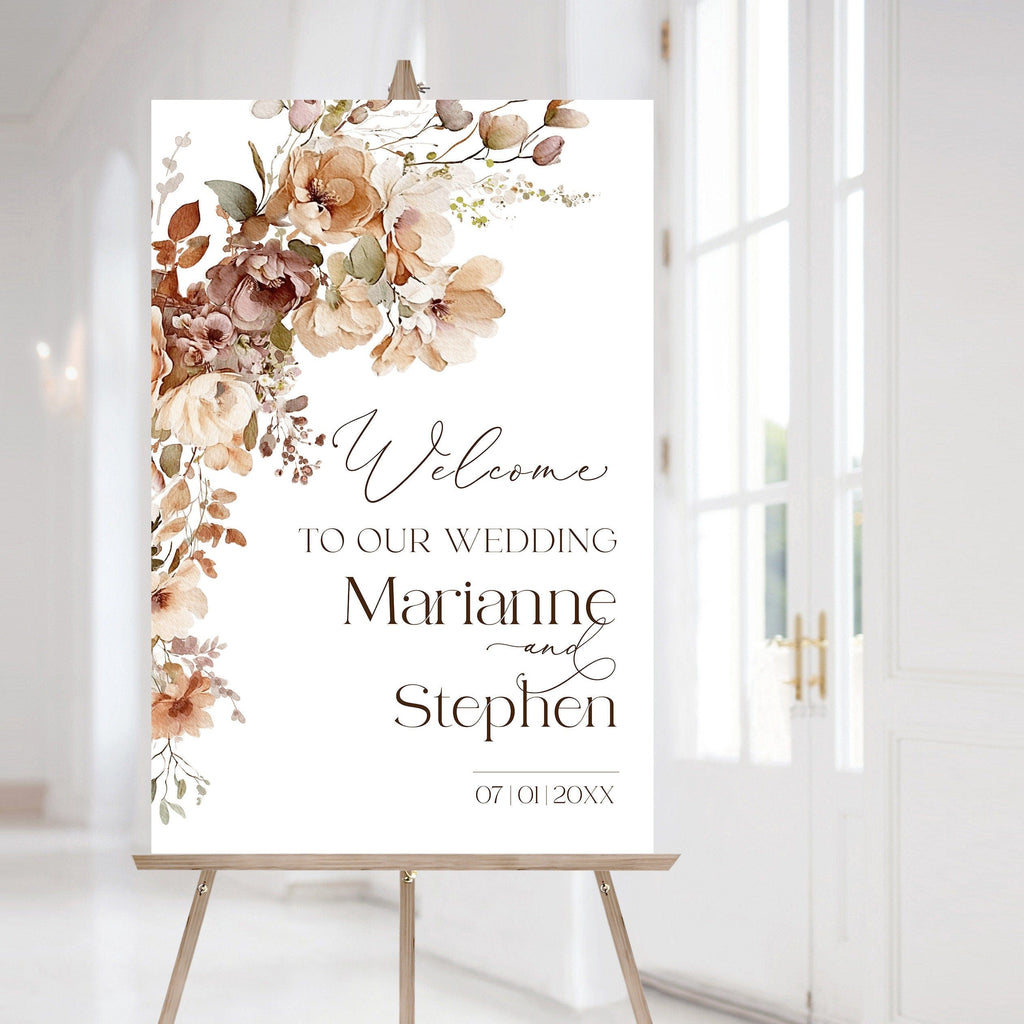 A wedding welcome sign with floral design, featuring the names of the couple and the text 'Welcome to our Wedding'. The sign is displayed on an easel in a bright room with a flower arrangement in the background.