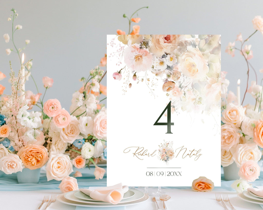 A table number card with a floral design, prominently featuring peach and other soft colors, displayed on a table with a bouquet of flowers in the background.