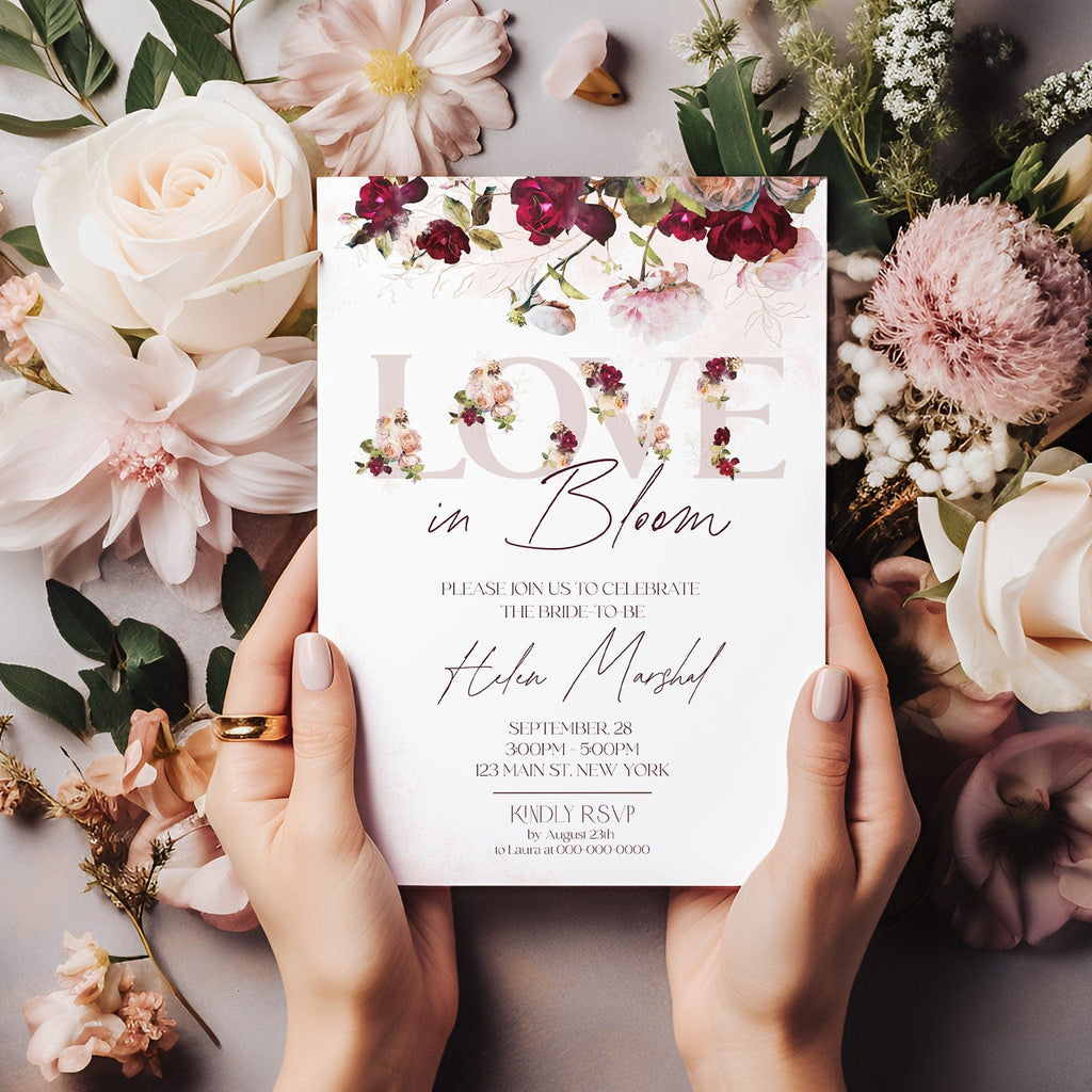A bridal shower invitation with a floral design, held in hands against a backdrop of various flowers including roses.