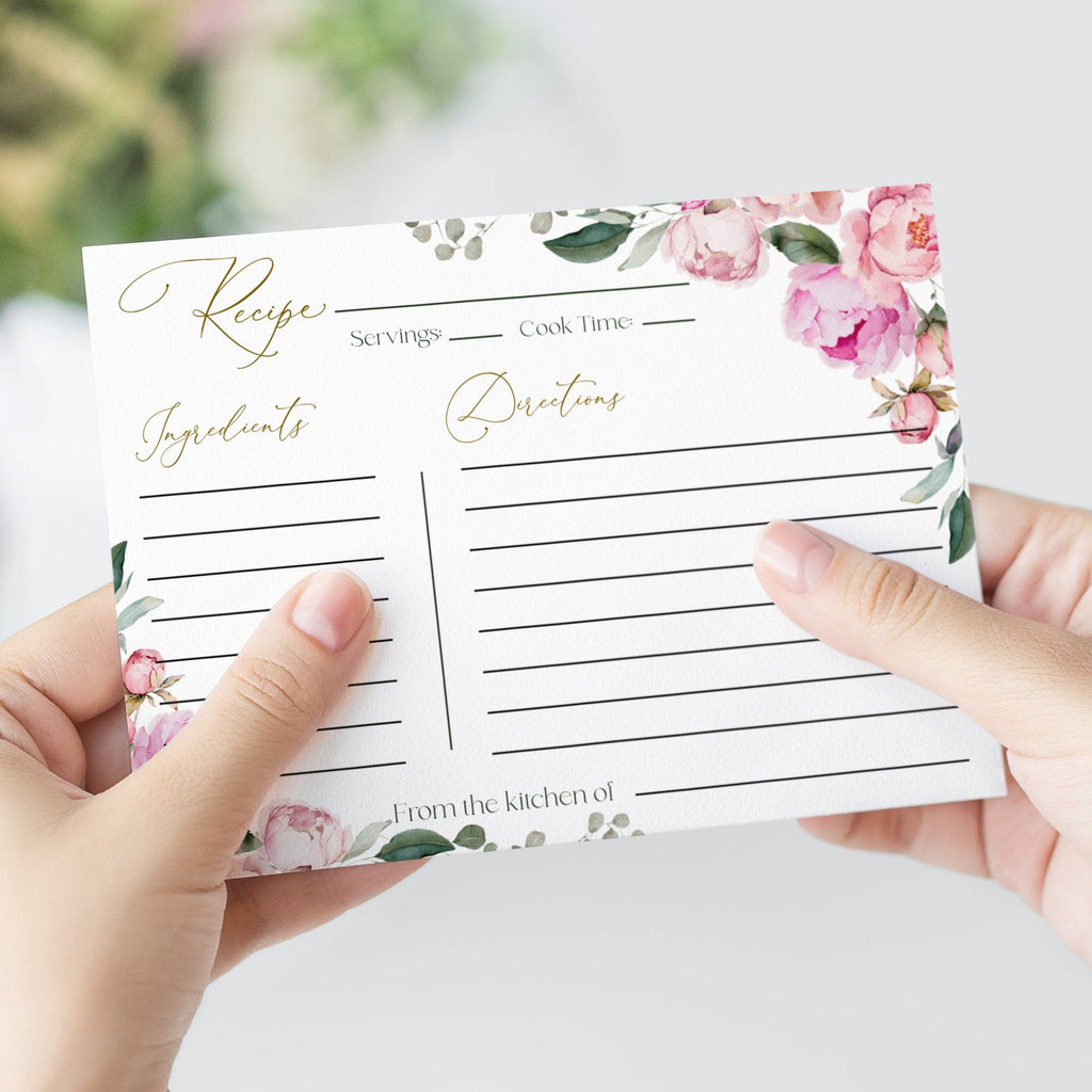 A hand holding a floral printable recipe card with the words 'Recipes' at the top, decorated with peony flowers and leaves.